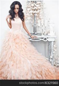 Fashionable portrait of beautiful lady in gorgeous couture dress in white interior. Holidays & Events. Evening dress. Princess dress. Christmas and New Year