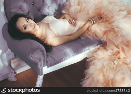 Fashionable portrait of beautiful lady in gorgeous couture dress on sofa