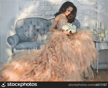 Fashionable portrait of beautiful lady in gorgeous couture dress on sofa. Holidays &amp; Events. Evening dress. Princess dress