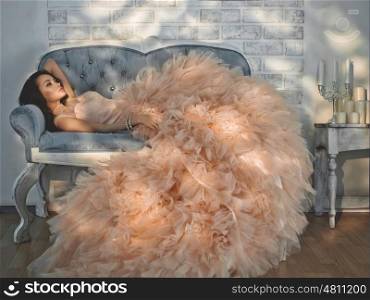 Fashionable portrait of beautiful lady in gorgeous couture dress on sofa. Holidays &amp; Events. Evening dress. Princess dress