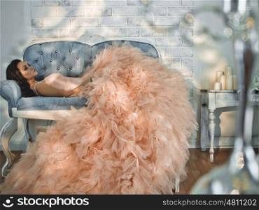 Fashionable portrait of beautiful lady in gorgeous couture dress on sofa. Holidays & Events. Evening dress. Princess dress
