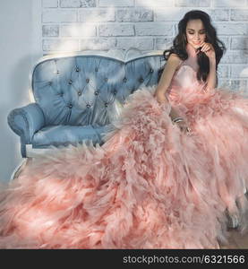 Fashionable portrait of beautiful lady in gorgeous couture dress on sofa. Holidays & Events. Evening dress. Princess dress. Christmas and New Year