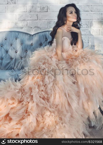 Fashionable portrait of beautiful lady in gorgeous couture dress on sofa. Holidays & Events. Evening dress. Princess dress. Christmas and New Year