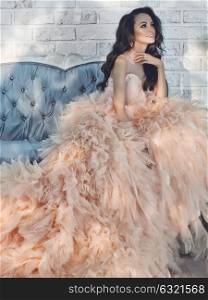 Fashionable portrait of beautiful lady in gorgeous couture dress on sofa. Holidays & Events. Evening dress. Princess dress. Christmas and New Year
