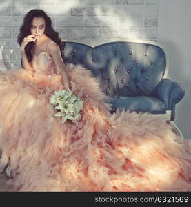 Fashionable portrait of beautiful lady in gorgeous couture dress on sofa. Holidays & Events. Evening dress. Princess dress. Christmas and New Year