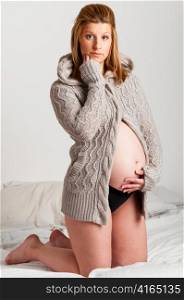 fashionable pregnant woman wearing woolen cardigan is looking at camera