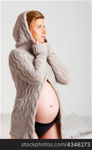 fashionable pregnant woman wearing woolen cardigan is looking sideways