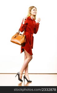 Fashionable pretty young woman wearing elegant casual red short dress and holding leather bag presenting stylish outfit.. Female wearing red dress holding bag