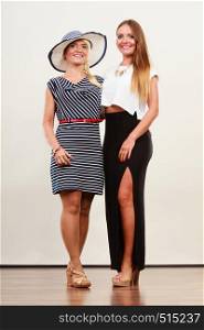 Fashionable style, clothes concept. Woman wearing white top and long black shirt showing her leg standing next to older female with short striped dress. Two women wearing fashionable dresses.