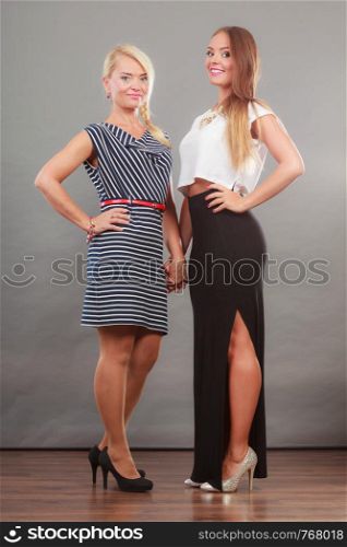 Fashionable style, clothes concept. Woman wearing white top and long black shirt showing her leg standing next to older female with short striped dress. Two women wearing fashionable dresses.