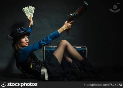 Fashionable subculture weapon concept. Steampunk girl with cash. Young gorgeous lady in victorian fashion lying on floor with banknotes briefcase and blunderbuss.. Steampunk girl with cash.