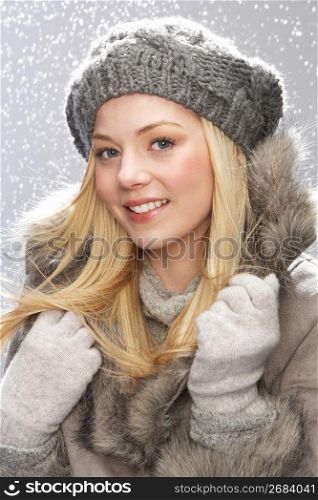 Fashionable Teenage Girl Wearing Cap And Fur Coat In Studio With Snow