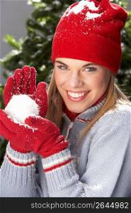 Fashionable Teenage Girl Wearing Cap And Knitwear Holding Snowball In Studio In Front Of Christmas Tree