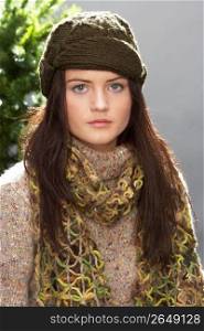 Fashionable Teenage Girl Wearing Cap And Knitwear In Studio In Front Of Christmas Tree