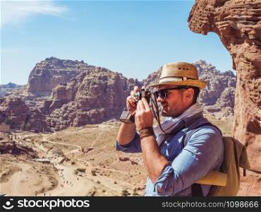 Fashionable tourist with a vintage camera, photographing the main attraction of the city of Petra in Jordan. Colorful photo. Concept of leisure, vacation and travel. Tourist with a vintage camera. Petra, Jordan.