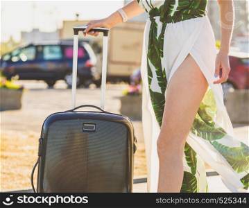 Fashionable woman arriving to new city wearing long dress, holding her suitcase on wheels admiring town after arrival.. Fashion model traveling to new city