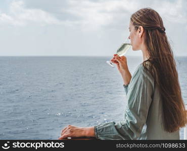 Fashionable woman holding a beautiful glass on the open deck of a cruise liner against the backdrop of blue sea waves. Side view, close-up. Concept of leisure and travel. Woman holding a glass on the deck