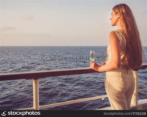 Fashionable woman holding a beautiful glass on the open deck of a cruise liner against the backdrop of blue sea waves. Side view, close-up. Concept of leisure and travel. Woman holding a glass on the deck
