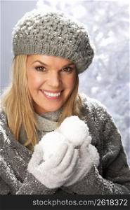 Fashionable Woman Wearing Cap And Knitwear Holding Snowball In Studio In Front Of Christmas Tree