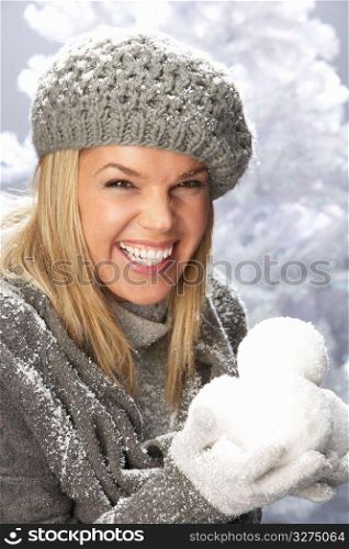 Fashionable Woman Wearing Cap And Knitwear Holding Snowball In Studio In Front Of Christmas Tree
