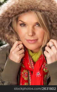 Fashionable Woman Wearing Parka Coat And Scarf In Studio In Front Of Christmas Tree