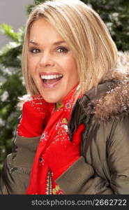 Fashionable Woman Wearing Parka Coat And Scarf In Studio In Front Of Christmas Tree