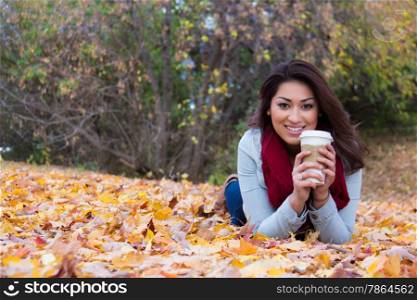 Fashionable woman with coffee lying down on autumn leaves