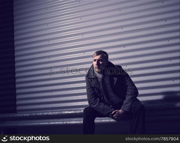 Fashionable young man wearing a warm overcoat, corrugated iron wall on background - cross processed image