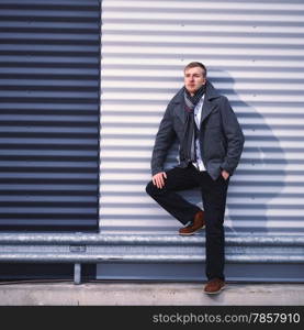 Fashionable young man wearing a warm overcoat, corrugated iron wall on background - cross processed image