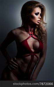 Fashionable young woman in red swimsuit with long curly hair. Bblonde posing in studio on black background