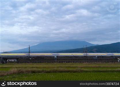Fast bullet train driving and passing Mountain Fuji near Tokyo railway station with green rice field at dusk, Japan