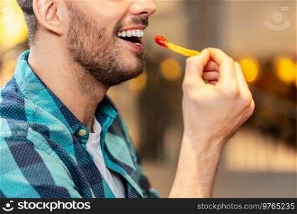 fast food and people concept - close up of happy man eating french fries with ketchup at restaurant. close up of happy man eating french fries