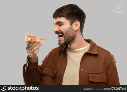 fast food and people concept - happy smiling young man eating pizza over grey background. happy smiling young man eating pizza