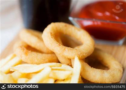 fast food and unhealthy eating concept - close up of deep-fried squid rings, french fries, coca cola and ketchup on wooden table
