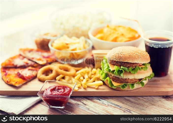 fast food and unhealthy eating concept - close up of hamburger or cheeseburger, deep-fried squid rings, french fries, drink and ketchup on wooden table