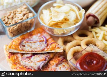 fast food and unhealthy eating concept - close up of pizza, deep-fried squid rings, potato chips, peanuts and ketchup on wooden table top view
