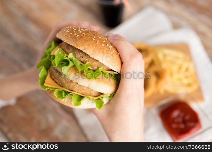 fast food and unhealthy eating concept - close up of woman holding hamburger. close up of woman holding hamburger