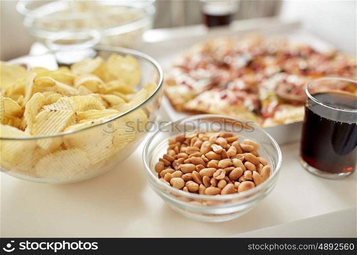 fast food and unhealthy eating concept - roasted peanuts, potato crisps and glass of cola drink on table