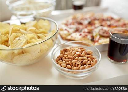 fast food and unhealthy eating concept - roasted peanuts, potato crisps and glass of cola drink on table