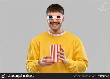 fast food, cinema and people concept - smiling young man in yellow sweatshirt and 3d movie glasses with popcorn in striped bucket over grey background. happy man 3d movie glasses with popcorn in bucket