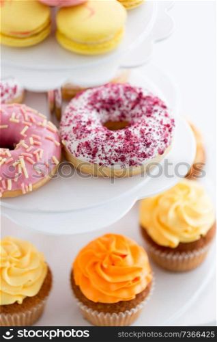 fast food, dessert and sweets concept - close up of glazed donuts and cupcakes on stand. close up of glazed donuts and cupcakes on stand
