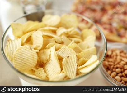 fast food, junk-food and unhealthy eating concept - close up of crunchy potato crisps in glass bowl and other snacks