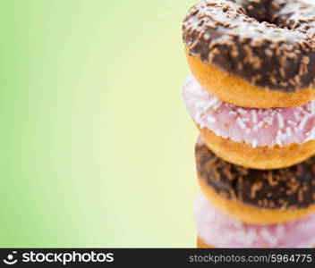 fast food, junk-food, baking and unhealthy eating concept - close up of glazed donuts pile over green background