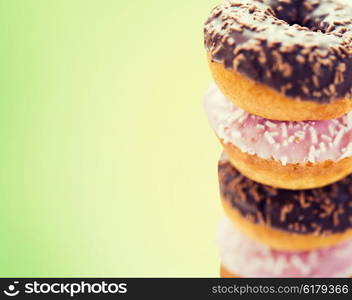 fast food, junk-food, baking and unhealthy eating concept - close up of glazed donuts pile over green background