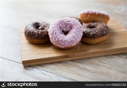 fast food, junk-food, baking, sweets and unhealthy eating concept - close up of glazed donuts on wooden board on table
