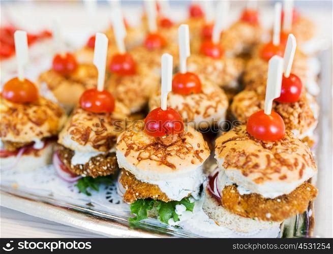 fast food, junk-food, catering and unhealthy eating concept - close up of canape hamburgers or sandwiches on serving tray