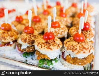 fast food, junk-food, catering and unhealthy eating concept - close up of canape hamburgers or sandwiches on serving tray
