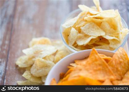 fast food, junk-food, cuisine and eating concept - close up of potato crisps and corn nachos in bowls on table