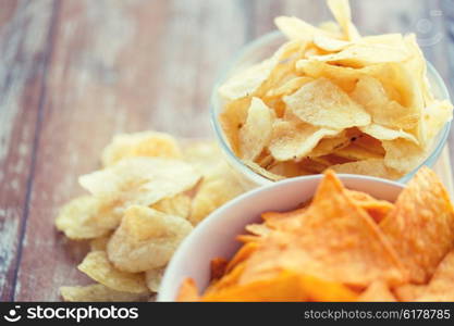 fast food, junk-food, cuisine and eating concept - close up of potato crisps and corn nachos in bowls on table