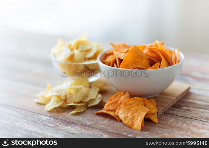 fast food, junk-food, cuisine and unhealthy eating concept - close up of crunchy potato crisps and corn crisps or nachos in bowls